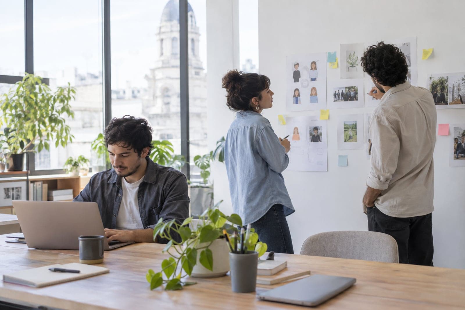 A marketing agency team reviews audience sketches on a wall while a colleague works on a laptop.