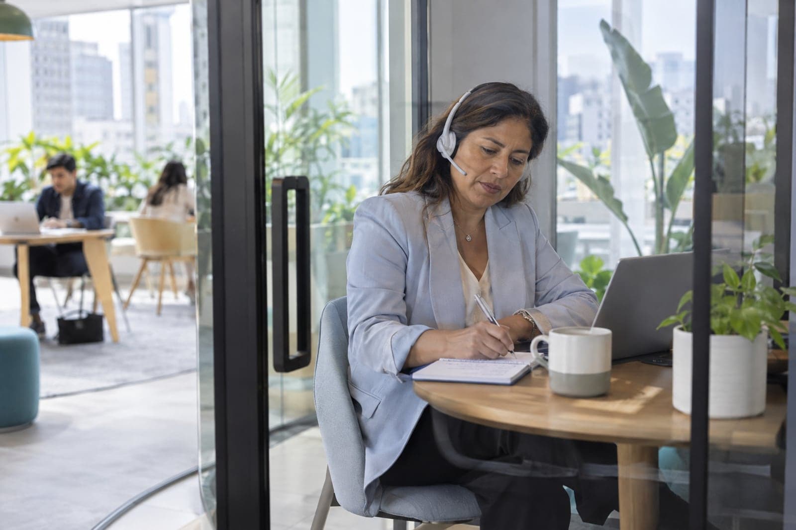 A recruiter with a headset takes notes during a video interview in a coworking phone booth.